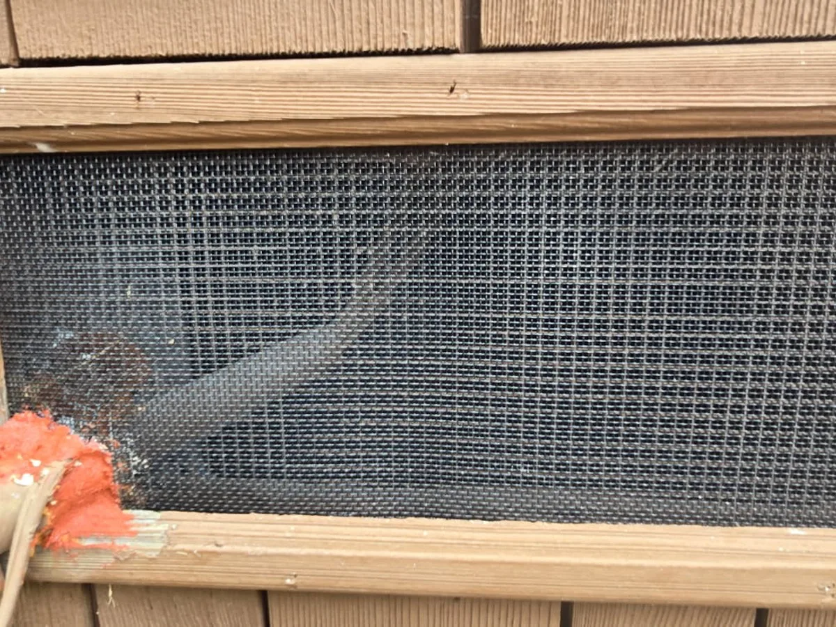 After: a completed vent with one-eighth-inch stainless mesh, reinstalled trim, and fire-rated caulking. Typical of all ten openings.
